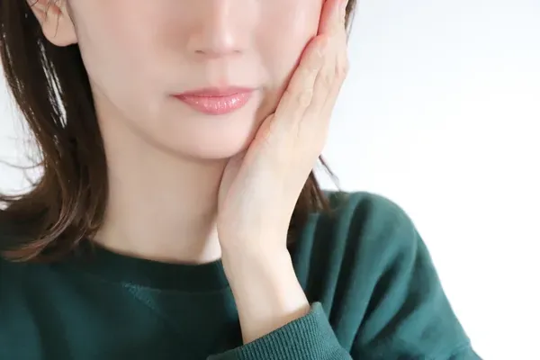 親知らずによる奥歯の痛みや腫れに悩んで頬を押さえている女性のイメージ画像
